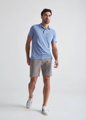 A person wearing a white t-shirt, DUER Live Free Journey Shorts in Titanium, and white sneakers stands with one hand in their pocket against a plain background.