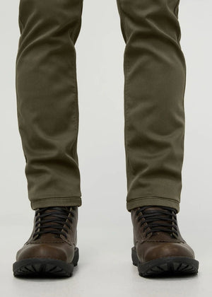 A person stands facing away from the camera against a plain background, wearing DUER - NO SWEAT ATHLETIC TAPER PANTS IN KELP paired with brown shoes.
