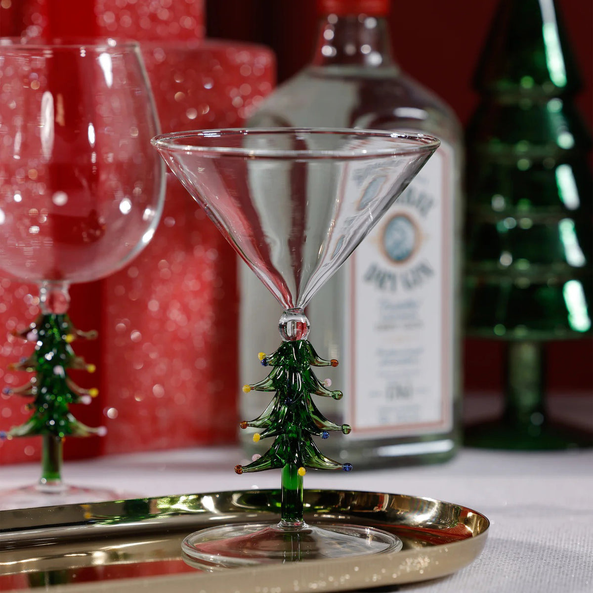 The ZODAX TREETOP CHEERS MARTINI GLASS features a clear bowl and a festive green Christmas tree stem with colorful ornaments, holding up to 5.07 oz—perfect for your favorite holiday cocktails.