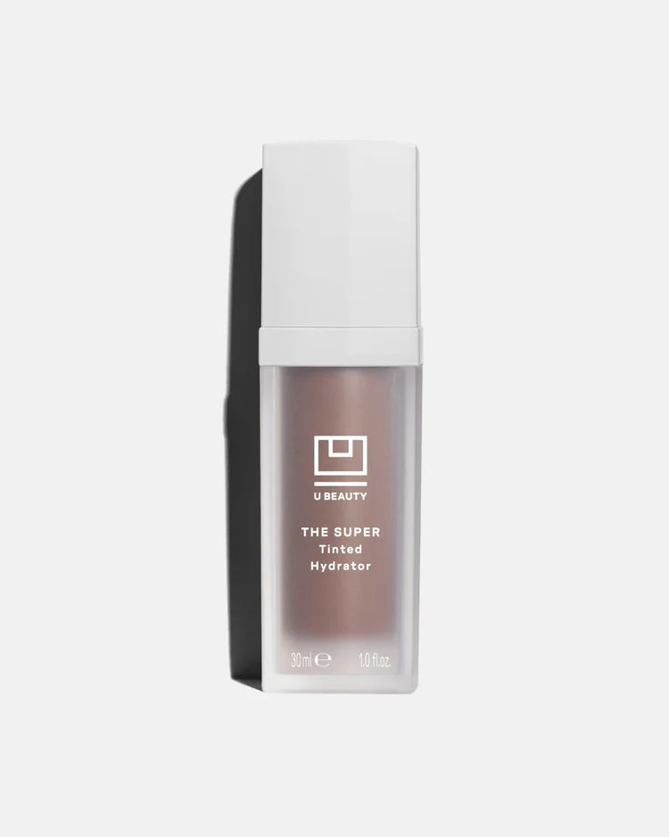 A 30 ml (1.0 fl oz) bottle of U BEAUTY - THE SUPER TINTED HYDRATOR SHADE 10, a dewy skin tint and moisturizer, stands upright with a white cap and frosted body against a light grey background.
