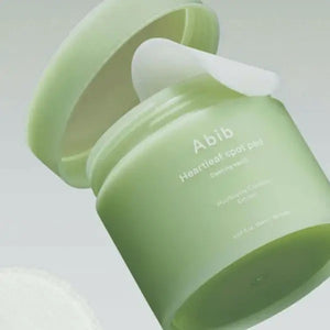 A light green jar labeled "ABIB - HEARTLEAF SPOT PAD CALMING TOUCH 80 PADS" from ASIAN BEAUTY WHOLESALE contains 80 pads with heartleaf extract and is shown against a plain white background.