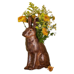The QUAIL CERAMICS - HARE VASE, LARGE by QUAIL DESIGNS is a hand-painted brown ceramic vase shaped like a hare, displayed with yellow and white flowers and greenery. A single yellow flower lies beside it on a white background.