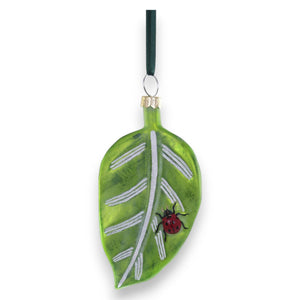 The CODY FOSTER GARDEN FRIENDS ORNAMENT is a charming glass leaf with white veins, a red ladybug detail, and a dark green hanging ribbon—perfect for any nature lover’s collection.