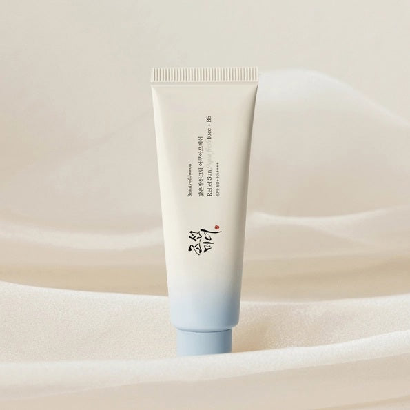 A tube of KOSMIC KBEAUTY SKINCARE BEAUTY OF JOSEON - RELIEF SUN SUNSCREEN, AQUA FRESH SPF 50+ is positioned on and next to four ice cubes containing embedded flowers, set against a crisp white background.