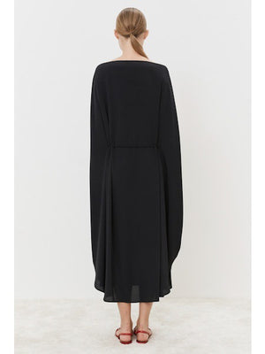 A person stands gracefully on a light-colored floor, wearing the MEIMEIJ Silk Blend Dress with cape-like sleeves, showcasing a modern classic look. The outfit is paired with red, open-toed flat shoes against a simple white backdrop.