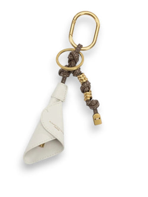 The GIANNI CHIARINI CALIA CHARM KEY RING features gold-toned rings and clip, a brown knotted synthetic leather detail, gold accents, a small lock charm, a Calia charm, and a folded white leather piece.
