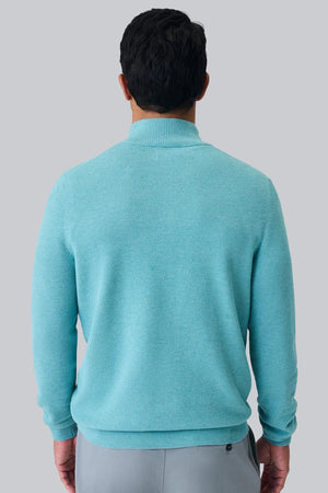 A man with short dark hair wears the MACK WELDON TECH LINEN QUARTER ZIP in Deep Lagoon Heather over a white shirt and light gray pants, standing against a plain white background with his hands loosely clasped.