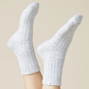 Two feet in SOFTIES - MARSHMALLOW CREW SOCKS IN HEATHER GREY are raised against a plain beige background. These ribbed, heather grey SOFTIES socks look ultra-soft and comfortable—perfect for lounging.