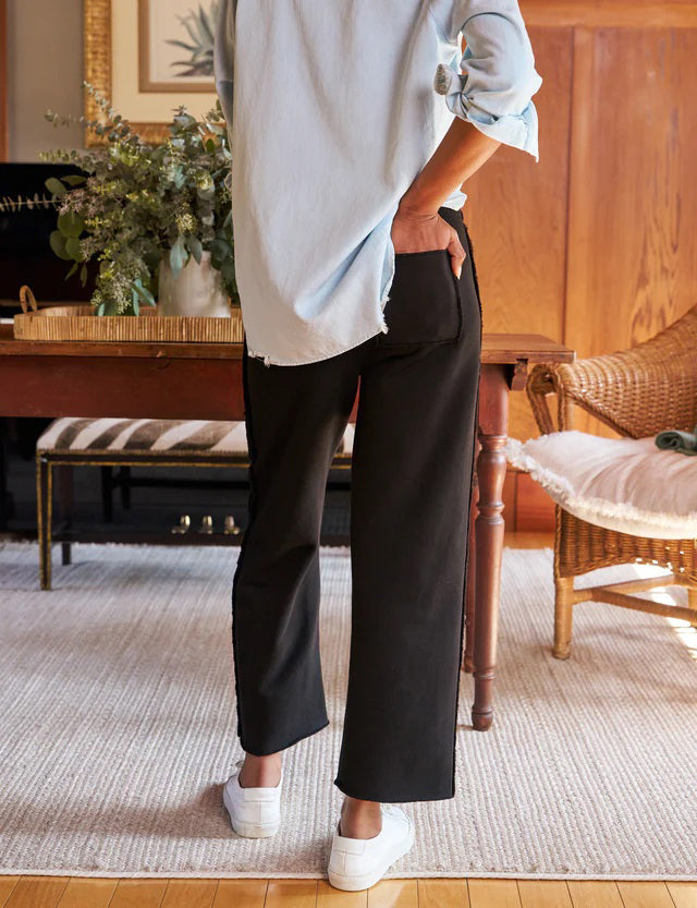 A pair of FRANK &amp; EILEEN - BELLA ITALIAN SWEATPANT IN BLACK from FRANK &amp; EILEEN featuring a mid-rise drawstring waist. The pants have a straight-leg cut with a slightly loose fit and a clean hem at the bottom. Made from Triple Fleece fabric, they appear smooth and comfortable, perfect for casual wear. The background is a plain white textured surface.