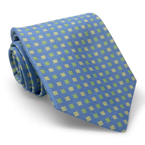 Introducing the PETER-BLAIR - BESPOKE SMALL SQUARES SILK TIE IN BLUE by BIRD DOG BAY: a rolled navy blue woven silk tie, artfully detailed with a pattern of small yellow and green squares on a white background.