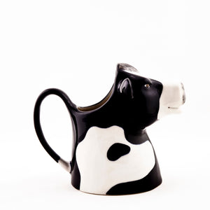 The QUAIL DESIGNS QUAIL CERAMICS - FRESIAN COW JUG MEDIUM features a black and white cow’s head and body, a looped handle, and top opening for pouring. This handpainted stoneware jug is dishwasher safe and easy to clean.
