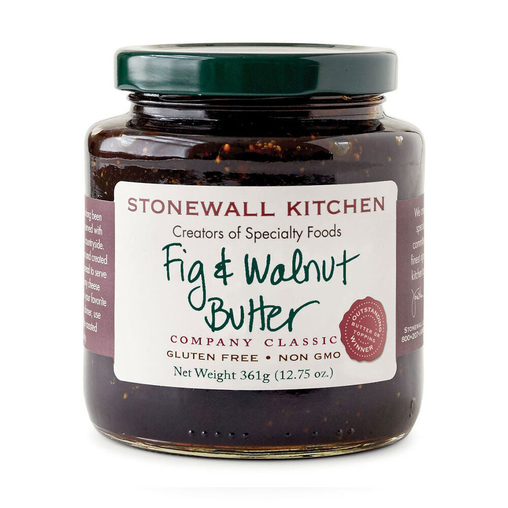 A glass jar of STONEWALL KITCHEN - FIG AND WALNUT BUTTER with a dark green lid. The label, showcasing culinary expertise, specifies that it is gluten-free and non-GMO, weighing 361 grams (12.75 oz). The text "Creators of Specialty Foods" is prominently displayed alongside illustrations of figs and walnuts—a true pantry essential.
