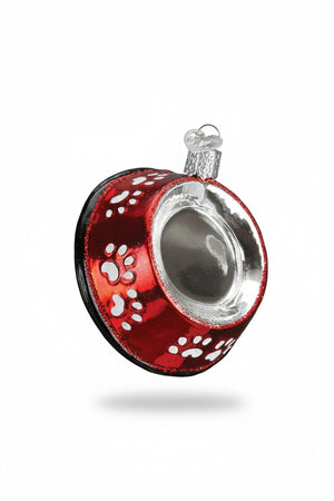 An OLD WORLD CHRISTMAS DOG BOWL ORNAMENT that is red, bowl-shaped, and decorated with white paw prints.