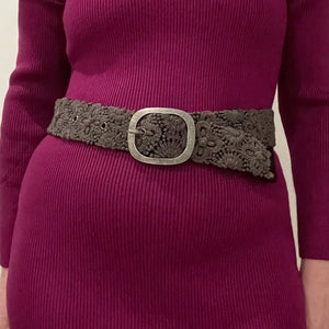 The JENNY KRAUSS - MIDNIGHT OASIS BELT features intricate raised floral embroidery, a round metal buckle, and a dark brown design, handcrafted in Peru and shown coiled on a light background.
