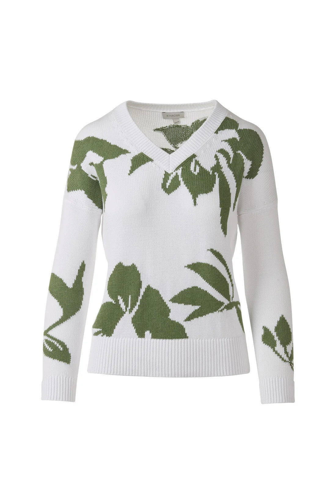 A woman faces forward wearing the KINROSS CASHMERE Intarsia Easy Vee Neck Cotton Sweater, featuring green leaf patterns. Her hair is up, and she pairs it with light blue jeans against a plain white background. 100% cotton by KINROSS.