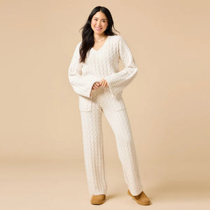 A woman wearing the SOFTIES CABLE KNIT MARSHMALLOW V-NECK WITH FLARED SLEEVE AND PANT SET, a marshmallow-soft, cream-colored cable knit v-neck sweater with wide sleeves and matching lounge pants.