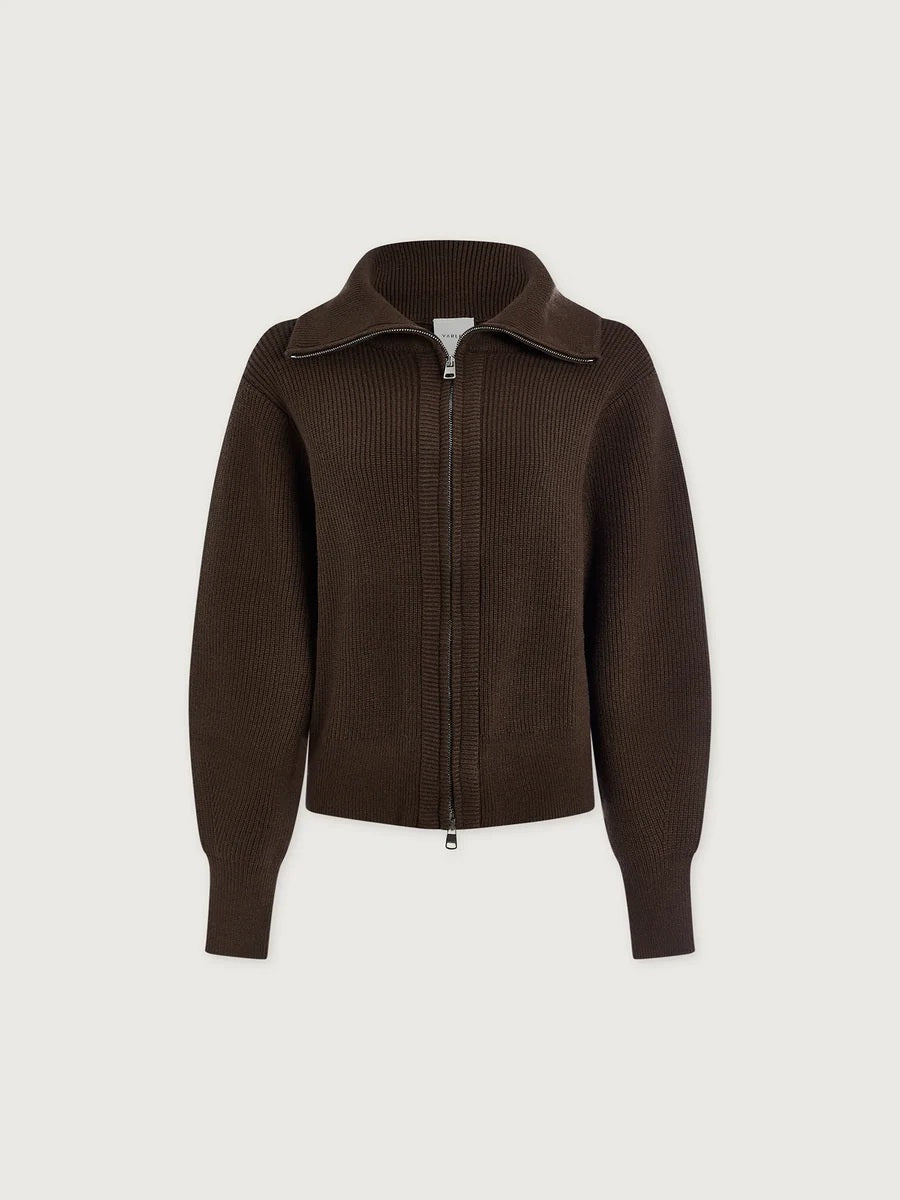 A person wearing a dark brown VARLEY - ENRICO ZIP-THROUGH KNIT JACKET featuring a ribbed soft viscose knit, a high collar, and a front zipper, ideal for cool weather layering.