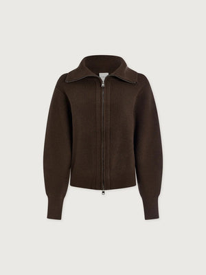 A person wearing a dark brown VARLEY - ENRICO ZIP-THROUGH KNIT JACKET featuring a ribbed soft viscose knit, a high collar, and a front zipper, ideal for cool weather layering.