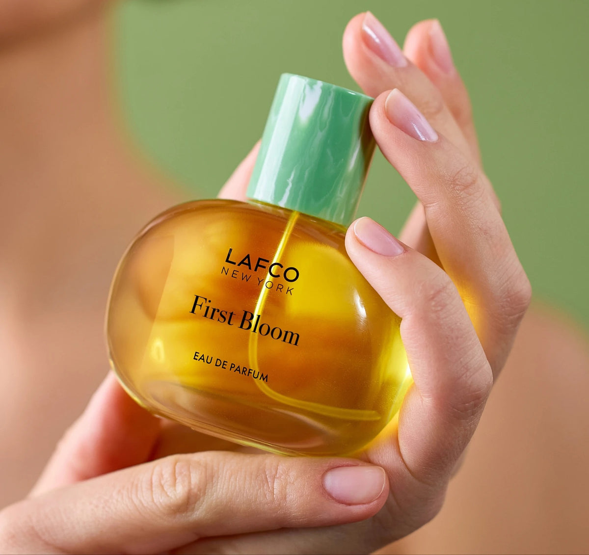 A box of LAFCO - FINE FRAGRANCE, FIRST BLOOM 50ML stands among white flowers and green vines against a pale beige background.