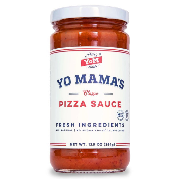 A clear glass jar of YO MAMA'S FOODS PIZZA SAUCE with a white lid showcases the No Added Sugar, keto-certified red sauce. The side label lists ingredients, nutrition facts, social media icons, and a bar code.