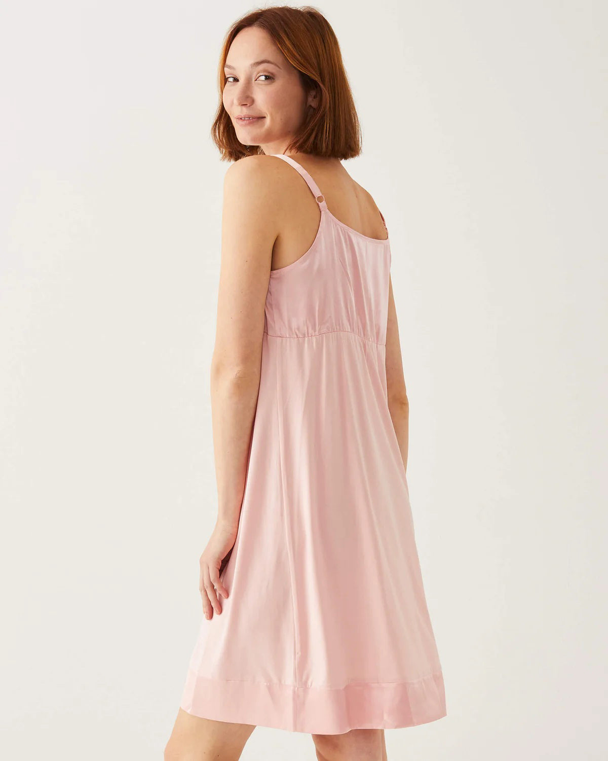 A woman stands against a white background wearing the MERSEA MOON DANCER PAJAMA DRESS in light pink with gray fuzzy slippers. With her short hair and relaxed look, it&#39;s perfect for cozy wedding pajamas or as a bride-to-be gift.