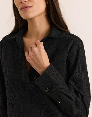 A woman wearing a HINSON WU - MONA LONG SLEEVE BONDED LACE SHIRT in black, paired with black trousers, black heels, and a black clutch.