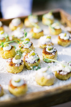 A close-up of a tray filled with small, round savory appetizers topped with a dollop of cream, green garnish, and a sprinkle of grated cheese, arranged neatly on a textured cloth.