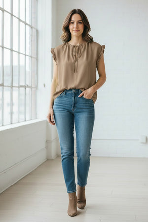 A woman wears the MEIMEIJ Cap Sleeve Blouse, a light green viscose top with ruffle cap sleeves and a tied neckline from MEIMEIJ, paired with white bottoms against a plain light background.