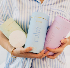 A light blue cylindrical container labeled “MUSEE - CALM BATH TABLETS” by MUSEE is positioned next to a stack of six white, round bath tablets. The container highlights the “Water Lily & Linen” scent, evoking the tranquil atmosphere of natural bath products ideal for a soothing soak.
