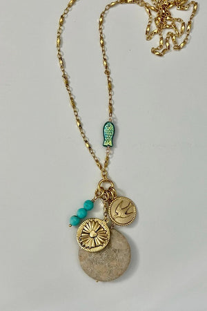 The SKYE NECKLACE by SANDRINE FRANCE STUDIO features a gold chain with a blue fish charm, turquoise beads, a bird-engraved gold coin, round gold charm, and a floral Fossil Coral pendant—a striking handmade jewelry piece.