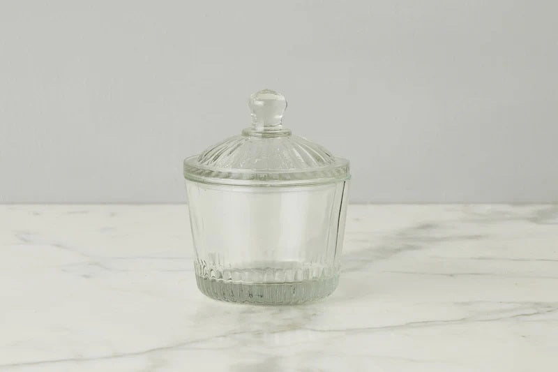 Two ETUHOME Bistro Glass Bon Bon Jars with ribbed lids sit on a wooden surface, one filled with yellow candies and the other nearly empty. Wrapped sweets are scattered nearby, creating a charming ETUHOME display.