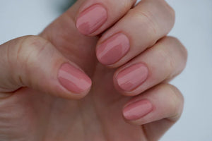 A glass bottle of TENOVERTEN - NAIL POLISH from the brand TEN OVER TEN, featuring a white cap and a dusty pink nail color. The front label displays "TEN OVER TEN" in white uppercase letters. This vegan, eight-free formula ensures both beauty and peace of mind. The background is plain and light-colored.