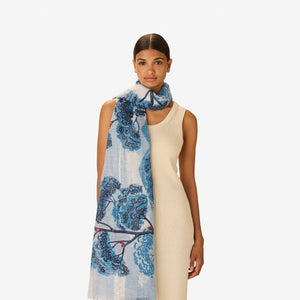 The INOUI EDITIONS AMBROISE SCARF IN DUCK BLUE by INOUI features an artistic blue and orange tree print on a light blue and white background, reminiscent of hand-printed linen cotton scarf blends.
