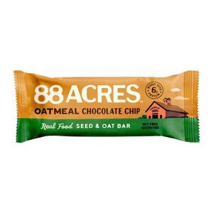 An 88 ACRES - OATMEAL CHOCOLATE CHIP SEED OAT BAR is shown on a light wooden surface, its brown and white wrapper featuring oats, chocolate chips, and Australian sea salt for a chewy cookie bar experience.