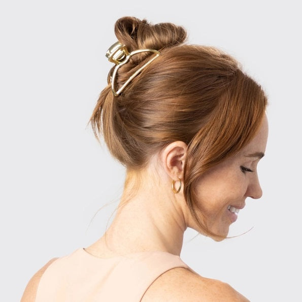 The KITSCH - OPEN SHAPE CLAW CLIP IN GOLD is a minimalist gold metal hair accessory from KITSCH, ideal for styling thick hair and showcased against a plain light background.