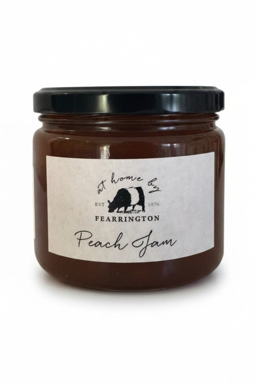 The FEARRINGTON SIGNATURE COLLECTION - FEARRINGTON HOUSEMADE PEACH JAM comes in a glass jar featuring a black lid and is adorned with a black and white striped ribbon. The white label reads "Peach Jam" and lists the ingredients as peach, vanilla, lemon, pectin, and sugar. Perfect as a hostess gift, it also notes that it is handmade by FEARRINGTON HOUSE and may contain allergens.