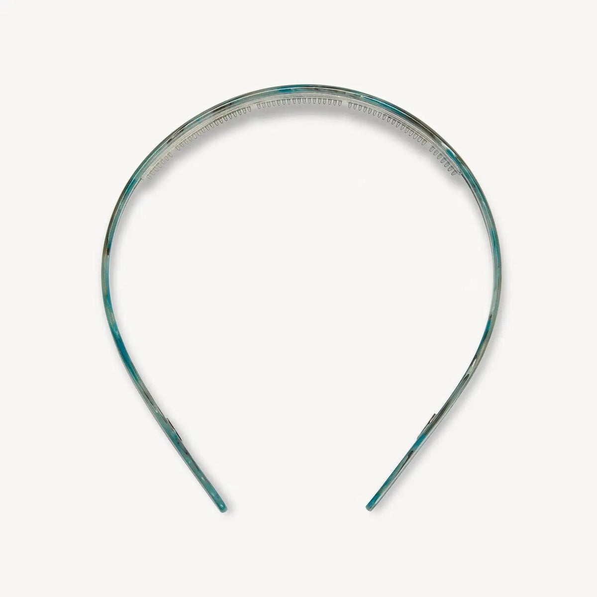 A young woman with wavy brown hair wears the MACHETE Ultralight Thin Headband in Jadeite and a gold hoop earring, gazing slightly past the camera with a neutral expression against a plain background.