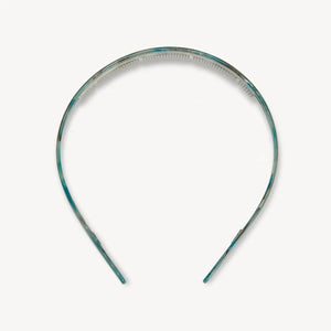 A young woman with wavy brown hair wears the MACHETE Ultralight Thin Headband in Jadeite and a gold hoop earring, gazing slightly past the camera with a neutral expression against a plain background.