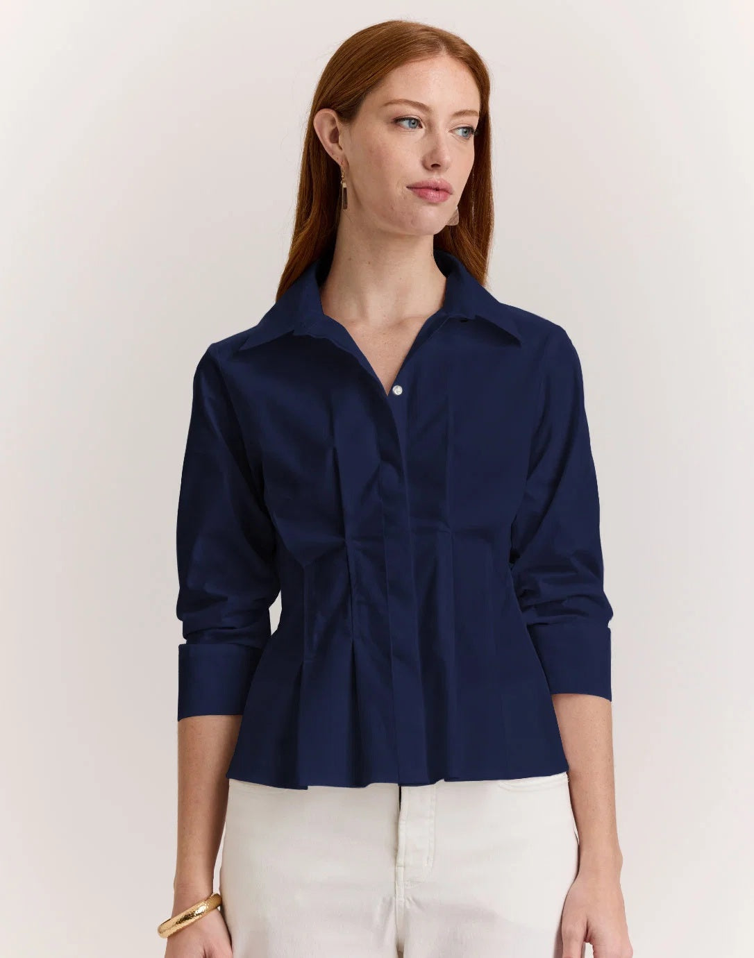 A woman with long red hair wears the HINSON WU - MARTINA 3/4 SLEEVE STRETCH POLISHED COTTON SHIRT IN NAVY, paired with white pants, standing against a plain light background.