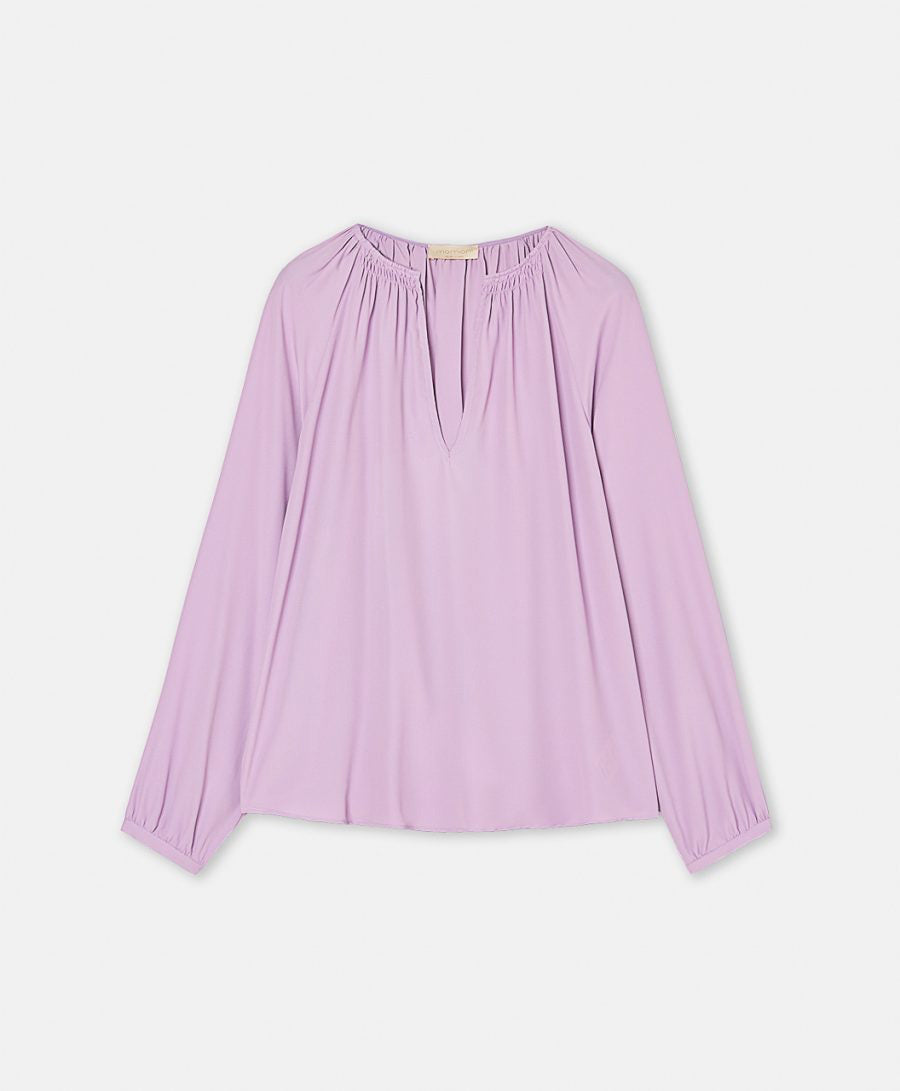 The MOMONI - LARICE SHIRT by MOMONI is a lavender-colored long-sleeve bohemian blouse with a gentle drape. It features a V-neckline, gathered detailing around the neck, and slightly elasticated cuffs. Crafted from luxurious viscose silk, this elegant piece is showcased laid flat against a white background.