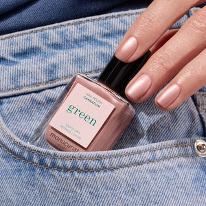 A bottle of MANUCURIST INC’s GREEN™ Nail Polish in the shade “Carnation,” featuring a black cap and pale pink color, with a label that reads “Quick Dry Intense Color.”.