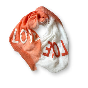 The OMBRE LINEN LOVE SCARF by CITRUS FASHIONS is dip-dyed in a two-tone palette of white and pink, with "LOVE" embroidered on both sections. Artfully crumpled into a circular swirl, it sits elegantly on a plain white background.