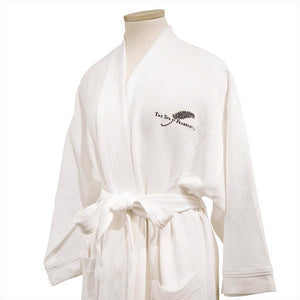 A folded white FEARRINGTON SIGNATURE COLLECTION - FEARRINGTON SPA ROBE from BOCA, with a belt tied in a knot, is displayed against a plain background. The kimono collar bathrobe features a black silhouette of a feather and "The Spa at Fairmont" embroidered on the chest.