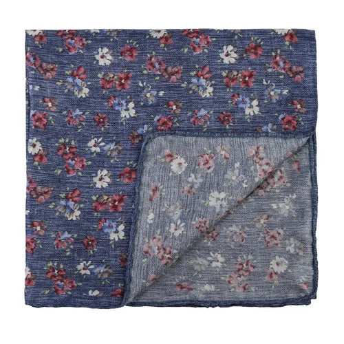 The AMANDA CHRISTENSEN Silk Pocket Square with Floral Pattern in Navy Melange features a sophisticated blue square design adorned with a red and white floral motif. One corner is artfully folded to reveal the reverse side, showcasing a subtly faded version of the same elegant pattern—making this refined accessory from AMANDA CHRISTENSEN the perfect addition to any collection of men’s accessories.