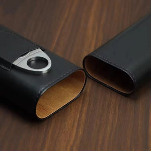 The AMERICAN LEATHER GOODS Leather Cigar Case with wood-lined humidor and cutter in brown sits on a wooden surface, while a black case rests behind. Leaf shadows appear on the wall in the background.