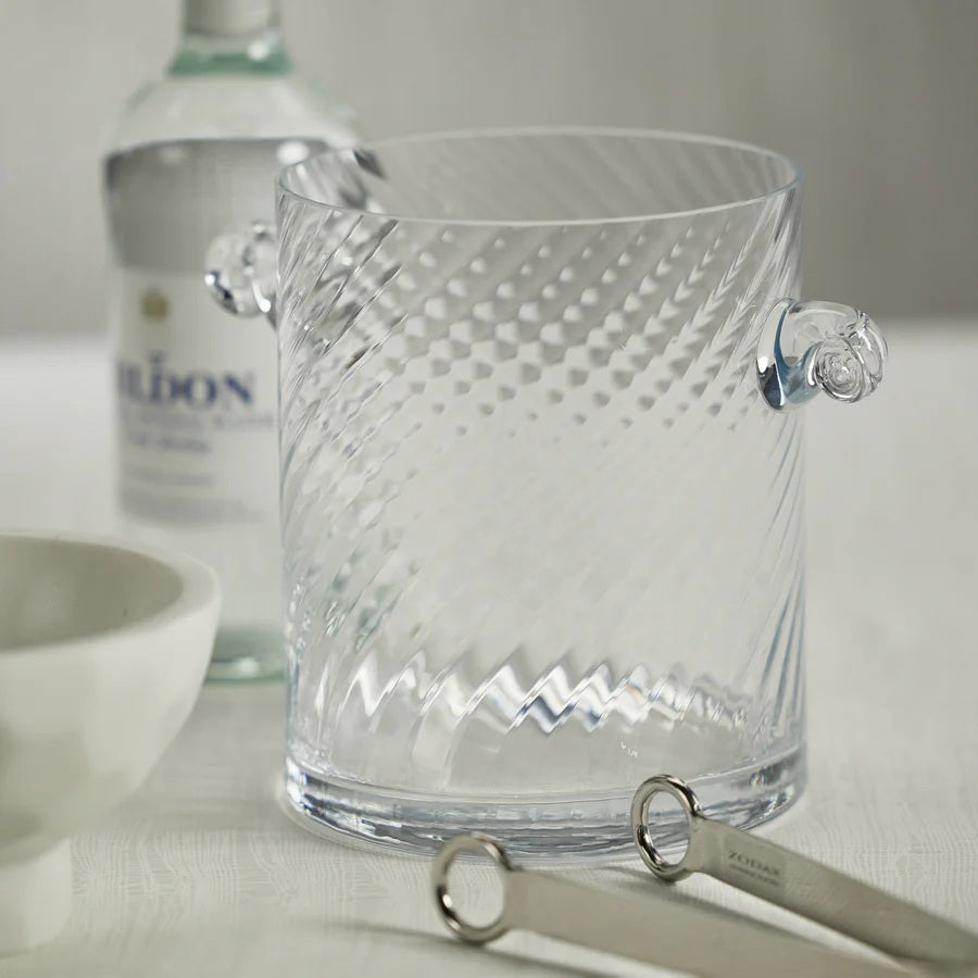 The BAGATELLE SWIRL GLASS ICE BUCKET by ZODAX features a clear, textured spiral design with diagonal swirls and two round handles—a modern bar accessory shown on a white background.