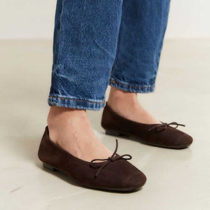 The REQINS HARMONY suede ballerina flats in Marron feature a dark brown finish and a small bow on the toe, shown in side profile against a plain light background—a timeless choice for any classic wardrobe.