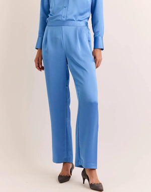 Model wears the HINSON WU - HOSTESS LIQUID SATIN PANT IN SKY BLUE by HINSON WU, featuring a relaxed straight leg and elastic waistband in luminous, light-catching sky blue satin. Styled with the matching long-sleeve top, they are pictured from the back against a neutral backdrop and complete the look with gray pointed-toe shoes.