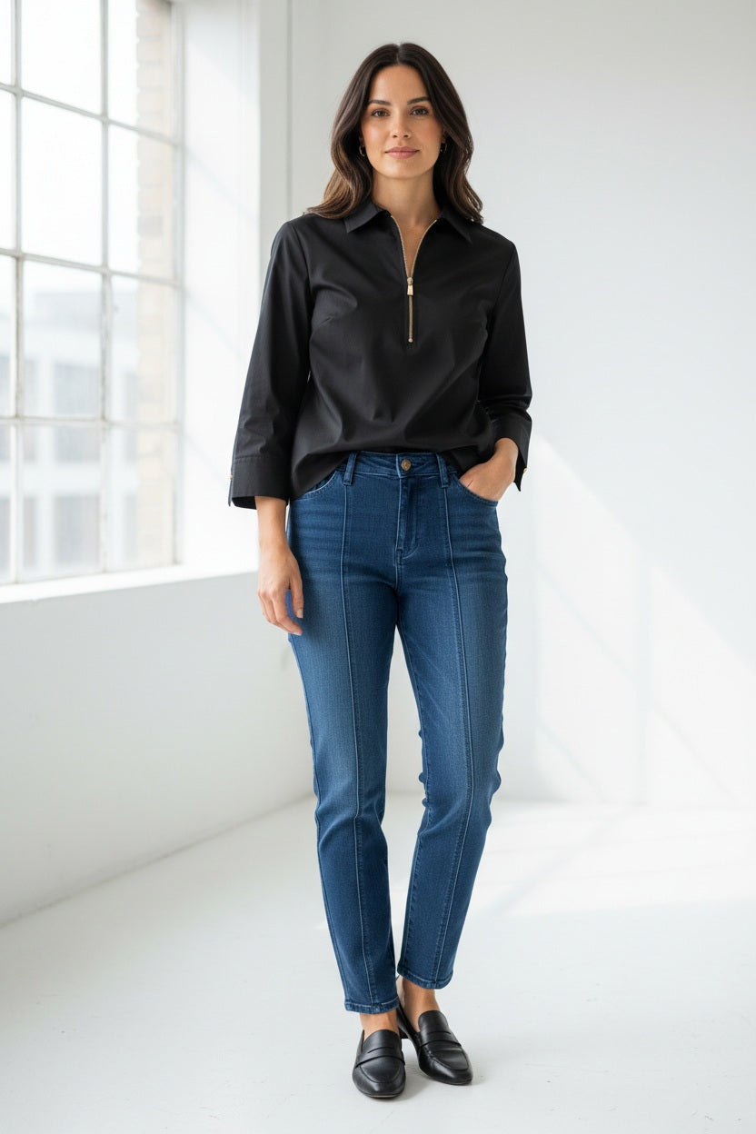 A woman with long brown hair is wearing the HINSON WU - ALESSA 3/4 SLEEVE SHIRT in black, crafted from stretch polished cotton, paired with blue jeans. She stands against a plain light background and looks at the camera with a neutral expression.