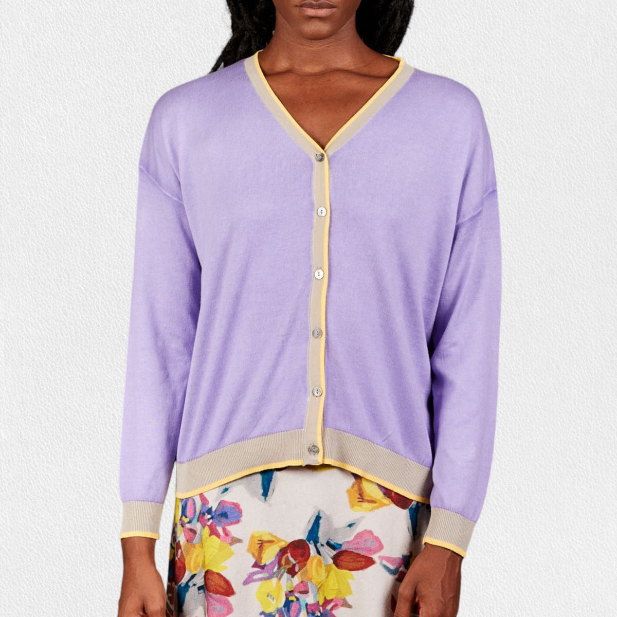 A woman wears the IN BED WITH YOU - BATWING SLEEVE CARDIGAN by IN BED WITH YOU/CLAUDIOLAI SRL, an orange V-neck with red and white trim, buttoned down the front, styled with multicolored patterned pants against a plain white background.
